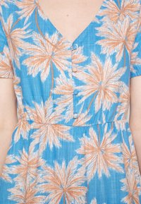 Robe bleue avec des motifs de feuilles de palmier marron et blanche, présentant un décolleté en V, des manches courtes, une taille élastique et des boutons recouverts de tissu sur le devant.