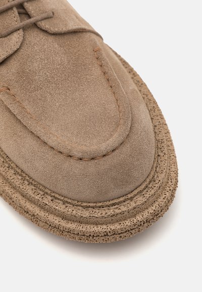 Suedesko i lysbrun med rund tå, synlig syning og tekstureret gummisål med lagdelt, perforeret design.