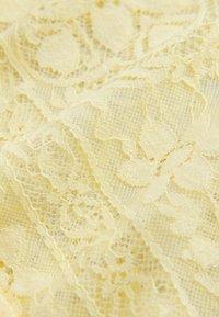 Dzeltenas mežģīnes audums ar ziedu rakstiem, kas izceļas ar smalku tekstūru un detalizētu izpildījumu, rādot atvērtu pinumu un viļņainas malas.