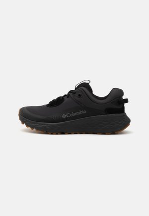 Shoe atlético preto da Columbia com uma superfície texturizada, colarinho acolchoado e sola de borracha com um padrão distinto para tração.