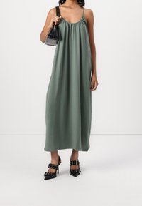Zelené, bezramínkové maxi šaty se nažehleným výstřihem. V kombinaci s lesklými černými lodičkami na vysokém podpatku se sponovými detaily a malou černou kabelkou.