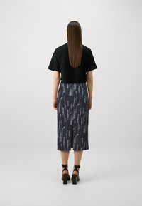 Fekete crop top, amelyhez egy mintás sötétkék midi szoknya van párosítva. A szoknya texturált mintázatú, oldalhasítékkal rendelkezik. Fekete magassarkú szandál.