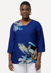 Blusa blu con scollo a V e maniche 3/4, caratterizzata da una grande stampa floreale in bianco e blu. Tessuto liscio, vestibilità ampia, adatta per un look casual.
