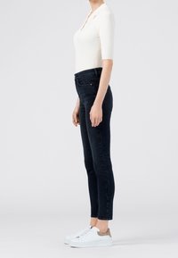 Top blanco de manga corta con canalé, combinado con jeans oscuros ajustados y zapatillas blancas con detalles en marrón, mostrado de lado.