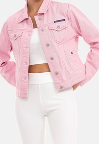 Rosa denimjacka med tryckknappar, två bröstfickor och sömdekorationer. Bärs över en vit ribbad topp och matchande hög midja byxor.