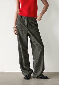 Pantalon large à rayures grises avec une finition texturée, assorti à un haut rouge vif sans manches et des chaussures noires. Design simple, tons neutres.