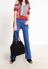 Top de hombros al descubierto con patrón rojo y negro, jeans acampanados azules y un bolso de ante negro. Zapatos negros de punta abierta con tacón ancho.
