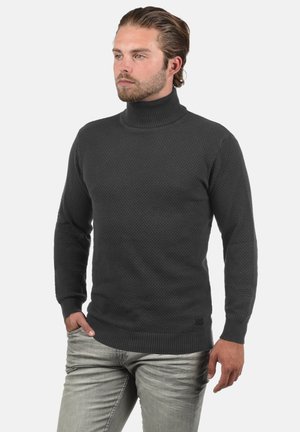 Pull en col roulé en charbon avec un motif en nid d'abeille texturé, des poignets et un ourlet côtelés, associé à un jean gris clair.