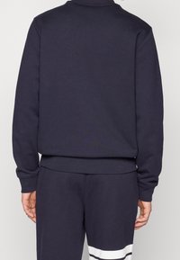 Marinblå sweatshirt med rund halsringning och ribbade ärmar, med en rak nederkant och mjuk textur. Matchas med matchande joggers.