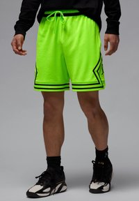 Shorts de sport vert fluo avec des accents noirs, une taille à cordon de serrage et une texture perforée, présentant des rayures horizontales et des motifs géométriques.