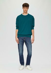 Teal sweater met een ronde hals en geribbelde manchetten, gecombineerd met donkerblauwe jeans en witte sneakers met een zwarte accent.