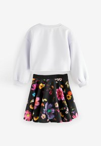 Ensemble à deux pièces composé d'un sweat-shirt court blanc et d'une jupe noire avec un motif floral vif dans différentes couleurs.