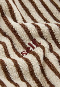 Roomkleurige en bruine gestreepte structuurstof met geborduurde rode letters die gedeeltelijk zichtbaar zijn op de plooien.