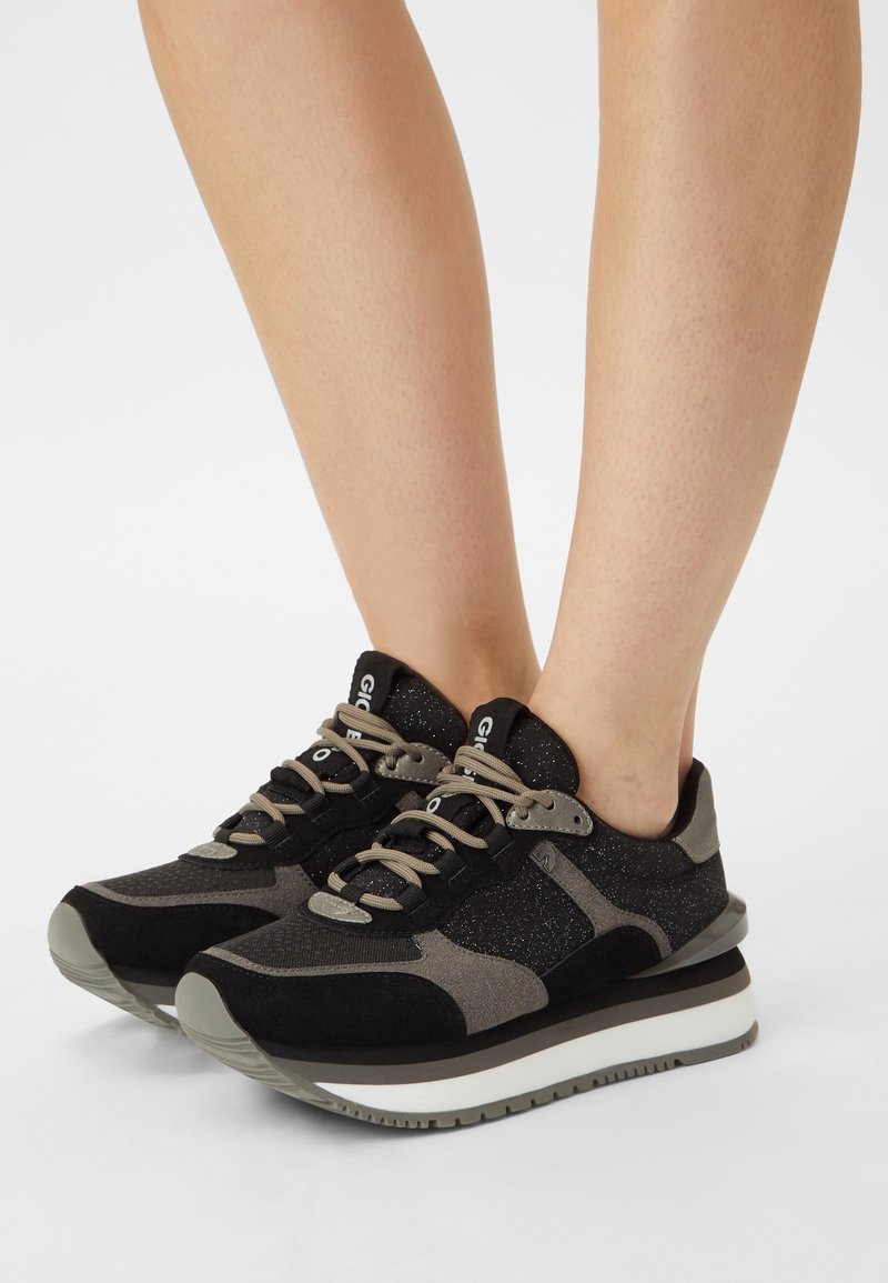 Zwarte en grijze sportschoenen met een mix van verschillende texturen, ronde veters, reflecterende accenten en een dikke witte zool.