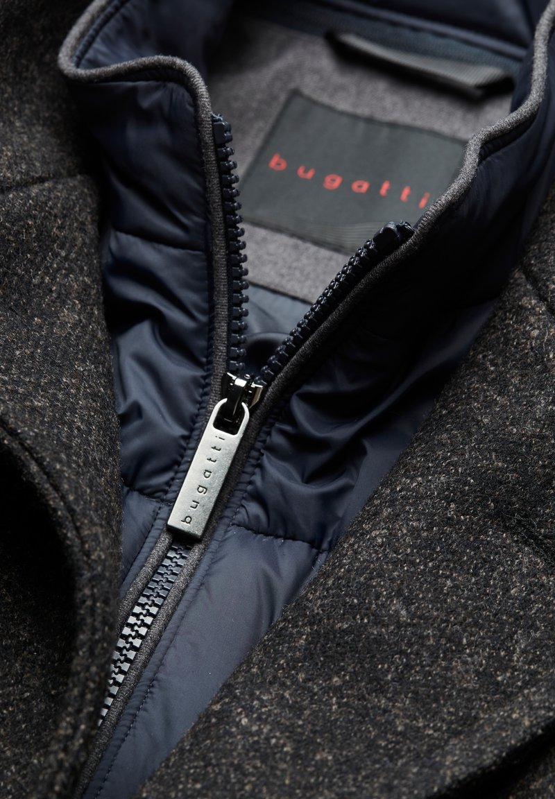 Veste en mélange de laine gris foncé avec un extérieur texturé ; doublure matelassée bleu marine ; elle comporte une fermeture éclair en métal avec un tirette de marque.