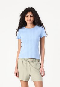 Lyseblå strikket kortermet topp med ribbestruktur og bølget kant, kombinert med beige shorts med snøring.
