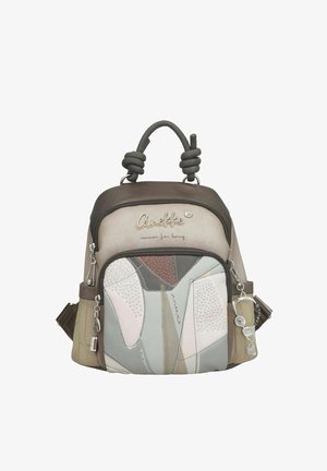 Petit sac à dos beige et marron avec poignée en forme de nœud, poche zippée avant présentant un design abstrait en patchwork, et porte-clés en forme de breloque métallique.