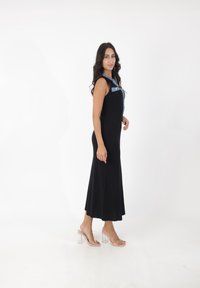 Zwarte geribbelde midi-jurk met een denimaccent op de schouder en zak; heeft een aansluitend lijfje en een uitlopende rok; gecombineerd met doorzichtige blockhakken.