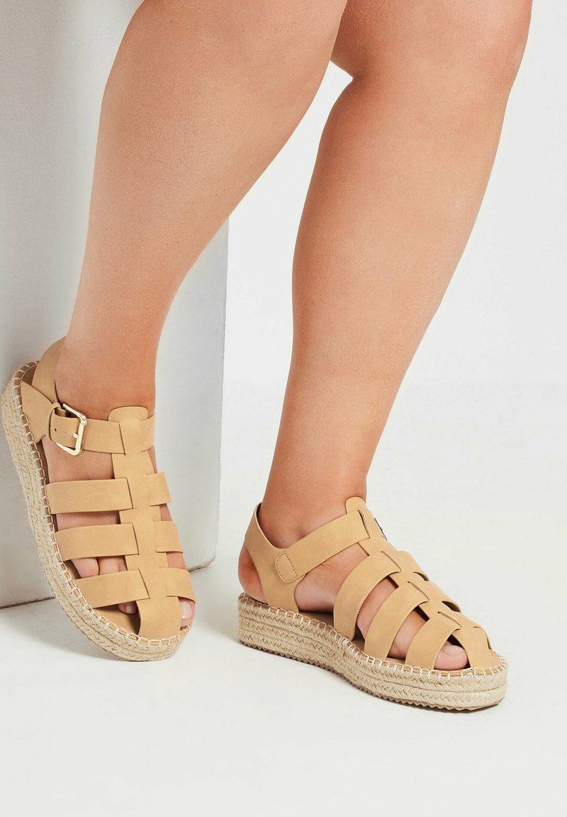 Sandali beige con fascette e suola a zeppa in juta intrecciata, dotati di dettagli a scomparsa e di una fibbia su una scarpa per una vestibilità regolabile.