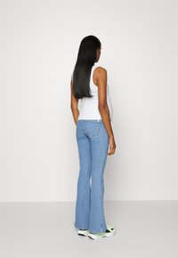 Top branco justo combinado com jeans azuis à boca de sino. Os jeans apresentam um tom de lavagem clara e um detalhe de costura discreto ao longo das laterais.