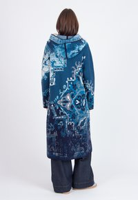 Hoody lange jas met een blauwe en witte gebreide patroon, met een relaxed fit en brede mouwen, gecombineerd met donkere denim broeken.
