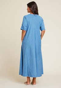 Lyseblå denim maxikjole med korte ermer, løs passform og sidelommer. Har en enkel rund hals og en rett kant.