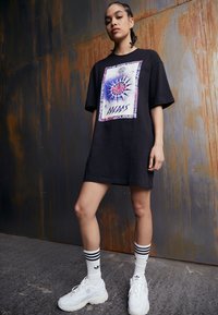 Black oversized t-shirt dress with a front graphic design featuring a compass and text. Worn with white socks and chunky white sneakers.
