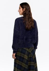 Granatowy, puszysty sweter z długimi rękawami i prostym krojem, zestawiony ze spódnicą w zieloną kratkę z granatowymi i musztardowymi akcentami.