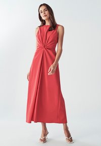 Malinovo červené šaty bez rukávov s prekrúteným predným detailom a plynulou maxi dĺžkou. Hladká tkanina a jemné záhyby vytvárajú pohyb.