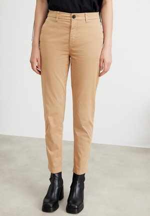 Tan cotton pants with a slim fit, featuring a front button closure and two side pockets, paired with black heeled ankle boots.