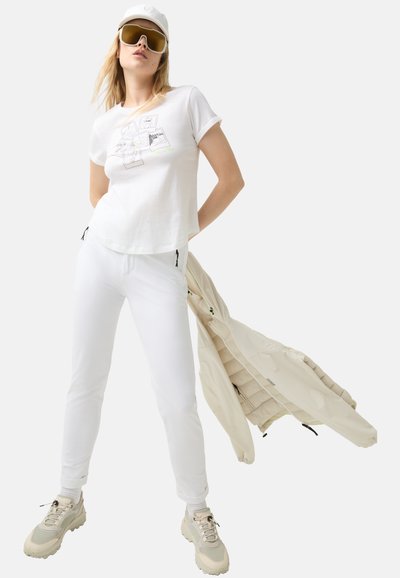 White cotton t-shirt with graphic front, paired with white slim-fit pants, beige puffer jacket, and light gray sneakers with textured soles.