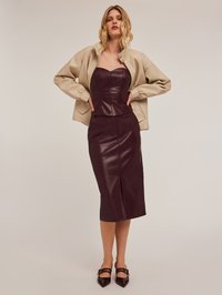 Abito in pelle bordeaux con corpetto aderente e dettaglio con spacco, abbinato a una giacca bomber beige. Tacchi a punta completano il look.