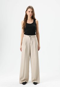 Zwarte geribde tanktop gecombineerd met beige, wijde broek met hoge taille, voorzien van een knoopsluiting aan de voorkant en twee zijzakken.