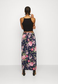 Top cropped preto combinado com uma saia longa de estampado floral em azul marinho, apresentando flores em rosa e verde. Saltos quadrados completam o visual.
