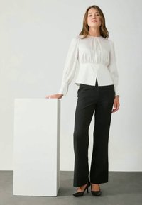 Blusa branca de manga comprida com textura franzida, cintura peplum; combinada com calças pretas evasê e sapatos pretos de salto alto.