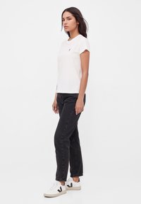 Witte katoenen t-shirt met korte mouwen en een klein logo, gecombineerd met zwarte denim jeans en witte sneakers met een zwart accent.