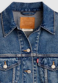 Κλασικό μπλε τζιν μπουφάν Levi's με γιακά, μεταλλικά κουμπιά, τσέπες στο στήθος και δερμάτινη ετικέτα επωνυμίας στην περιοχή  του γιακά.