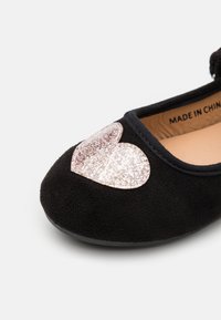 Ballerina nera in suede con un design a cuore luccicante rosa textures sulla punta. Sottile rivestimento interno e suola nera flessibile.