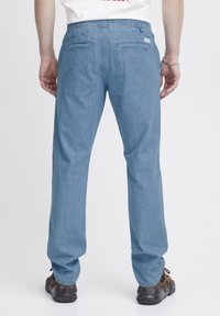 Pantalones de mezclilla azul claro con cintura elástica, dos bolsillos traseros y diseño de pierna recta. Llevados con zapatos oscuros, mostrados desde atrás.