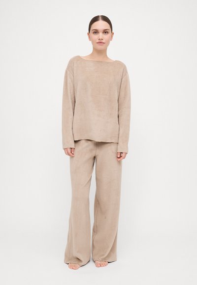 Beige fleece loungewear set featuring a loose-fitting long-sleeve top with a wide neckline and matching wide-leg pants. Soft texture throughout.