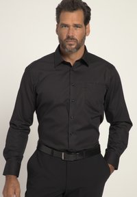 Schwarzes Langarmhemd mit Button-Down-Kragen und Brusttasche. Glatte Textur, taillierter Schnitt, kombiniert mit einem schwarzen Gürtel und Hosen.
