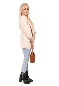 Beige Blazer, hellblaue Jeans und schwarze Stiefeletten. Hält eine braune Handtasche. Der Blazer hat umgeschlagene Ärmel und einen lockeren Schnitt.