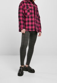 Pink and black plaid overshirt with button closures, paired with dark gray fitted leggings featuring a check pattern, and chunky black loafers.