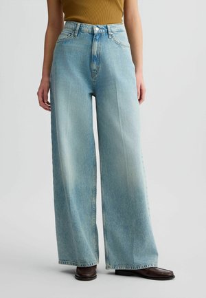 Lichtblauwe wijde jeans van denim. Heeft een hoge taille, een subtiele verwerkte afwerking en schone zomen. Gecombineerd met donkerbruine schoenen.