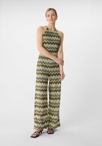 Halter neck jumpsuit in zigzag pattern featuring green, brown, and white tones. Flowy pants with a relaxed fit and textured fabric detail.