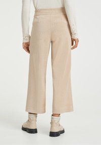 Bežové kordové kalhoty s širokými nohavicemi, strukturovaným povrchem a vysokým pasem, doplněné chunky světlými botami.