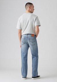 Lichtgrijs T-shirt met korte mouwen, blauwe denim jeans met een versleten look, rechte pasvorm en een rood merketiket aan de achterkant van de taille.