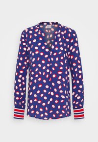 Marinblus med stora röda och vita prickar, V-ringning och randiga ärmslut. Tillverkad av ett lätt material med en mjuk textur.