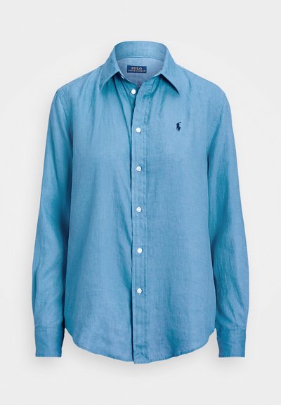 Light blue long-sleeve button-up shirt made of fabric with a slightly textured finish. Features a small dark logo on the left chest.