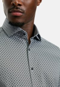 Button-up-Hemd in einem schwarz-weißen geometrischen Muster mit Spread-Kragen, strukturiertem Stoff und einer einzigen schwarzen Knopfschließe.